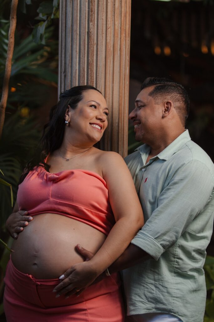 Pregnant couple embracing outdoors near a pillar